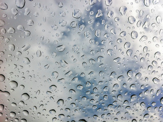Large clear rain drops on glass against a partly cloudy sky.