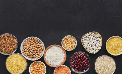 Legumes and grains in various bowls on black background