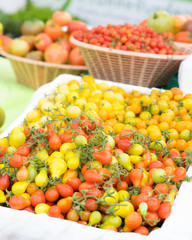Detail on a market stall of fresh tomatoes, with focus on orange cherry tomatoes in the foreground. Organic food concept.