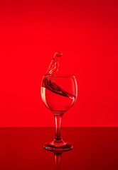 Splash of wine in a glass. Drink in glass on a red background.