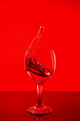 Splash of wine in a glass. Drink in glass on a red background.
