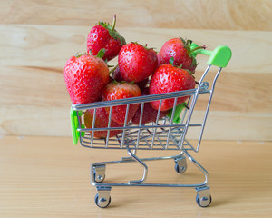 Red strawberry in blurred cart on blurred wooden background,