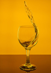 Splash of wine in a glass. Drink in glass on a yeallow background.