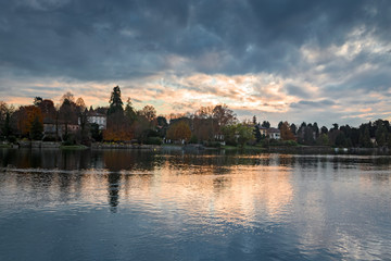 Panoramic view of the Ticino river with clouds and trees that are reflected in its clear water, on a winter day at sunset.
