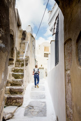 Fototapeta na wymiar Young woman walking in narrow residential alley; Santorini; Greece