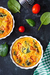 Frittata with fresh vegetables and spinach. Italian omelet in ceramic forms on a black background. Top view.