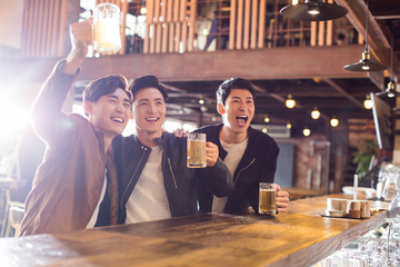 Happy young men drinking beer and cheering in bar