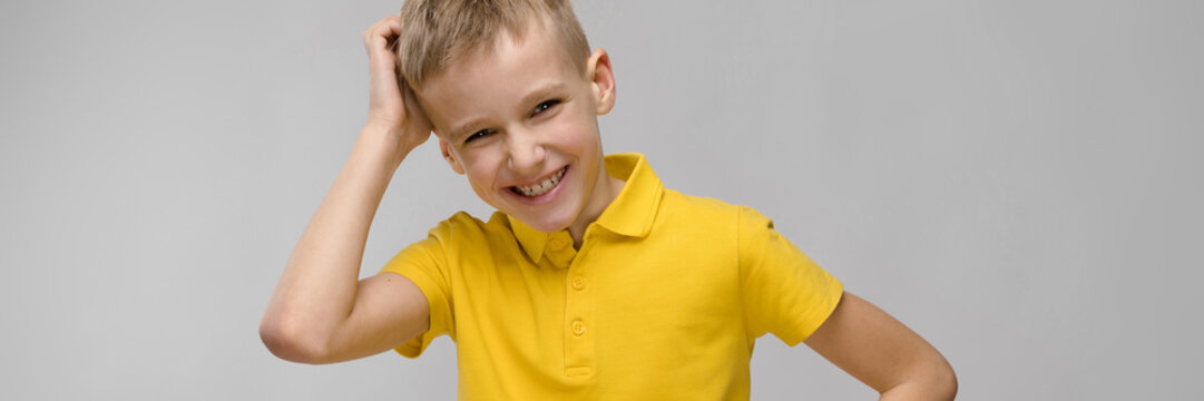 Portrait of cute little blonde caucasian boy in yellow t-shirt thinking on gray background