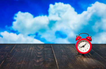 red alarm clock on a wooden table against a  blue sky