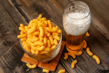 Crispy peanut puffs or flips snacks and cup of beer. Close-up on rustic vintage wooden table.