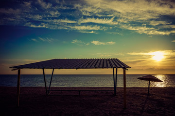 Canopy and old metal umbrella on an empty sandy beach at sunset.