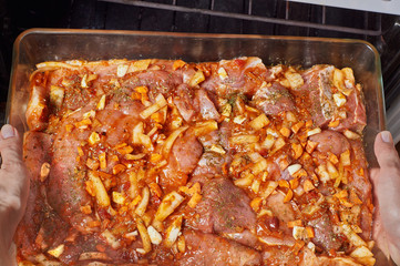 Woman prepares baking meat in a glass kitchenware on the background of the oven