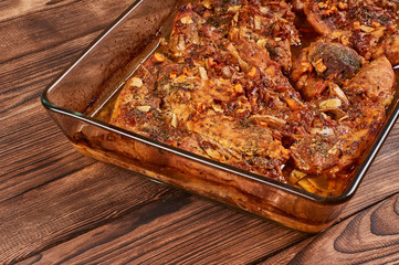 Juicy baked meat in a glass cookware on a brown wooden bakground, close-up