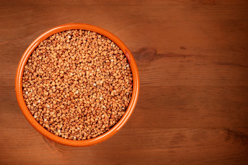 Dry buckwheat in a rustic earthenware bowl, shot from aboveon a dark rustic wooden background with copyspace
