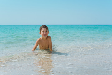 Fototapeta na wymiar A cheerful kid on the beach lies in the clear sea water.