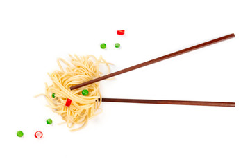 An overhead photo of chopsticks with udon noodles in a nest shape, green peas and red peppers, shot...