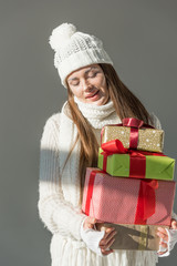 attractive woman in fashionable winter sweater and scarf holding presents isolated on grey