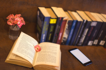 an open book with open pages and mobile phone and flower and books in background a relaxing scene in brown toning