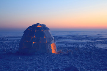 A snowy house called an igloo at sunset.
