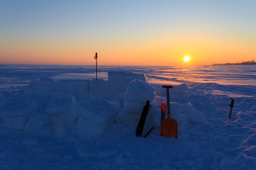 Unfinished igloo at sunset. In the snow blocks stuck tools for building a home.
