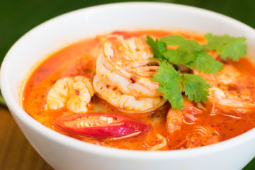 Thai spicy shrimp soup coconut milk (Tom Yum Kung) in a bowl with banana leaf in the background.