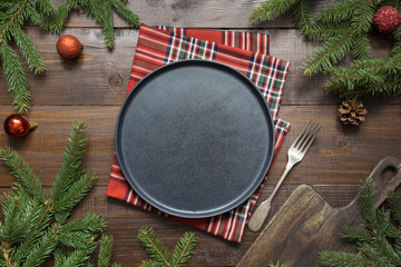 Christmas food border with black plate, evegreen branches, and red decor on wooden board. Space for...