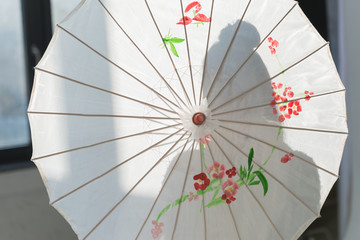 silhouette of woman standing with white japanese umbrella near window