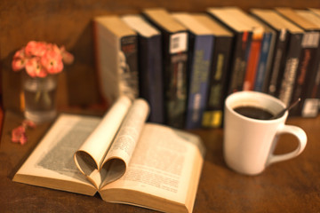 an open book with pages heart silhouette and coffee and flower and books in background a relaxing scene in brown toning