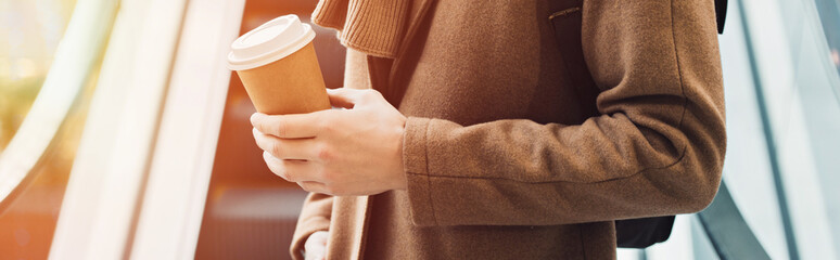 cropped view of man in warm clothing standing on escalator and holding disposable cup