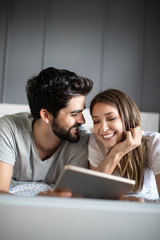 Happy young couple looking a tablet together and laughing while lying on the bed