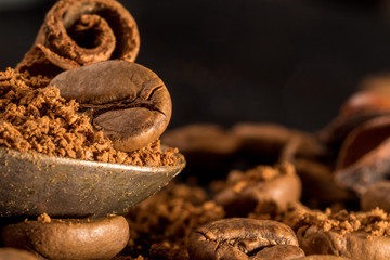 stick of cinnamon with a vintage spoon of ground coffee. coffee with spices. Food background on dark stone table. Macro close-up image.