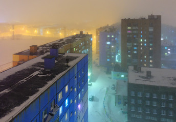 Top view of the night city. Snowfall and foggy mist on a cold winter late evening in the arctic. Colorful street lighting of a large northern city. Norilsk, Krasnoyarsk region, Siberia, Russia.