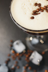 Glass with coffee drink, white crema, coffee beans, black background, ice cubes. Close up. Top view