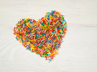 Candy sprinkles form heart shape. Multicolored heart-shape from candy confetti on white wooden...