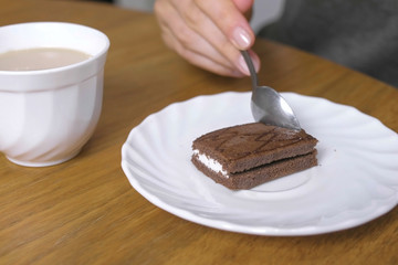 Woman is eating a piece of chocolate cake and drinks coffee. Close-up hand.