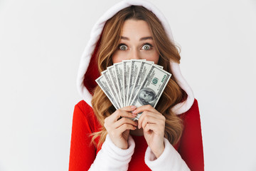 Portrait of european woman 20s wearing Santa Claus red costume smiling and holding fan of money in dollar banknotes, isolated over white background