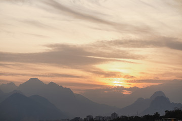Dramatic golden sunny evening cloudscape with misty high mountains, cityscape and golden cloudy calm sunset sky. Horizontal color photography.