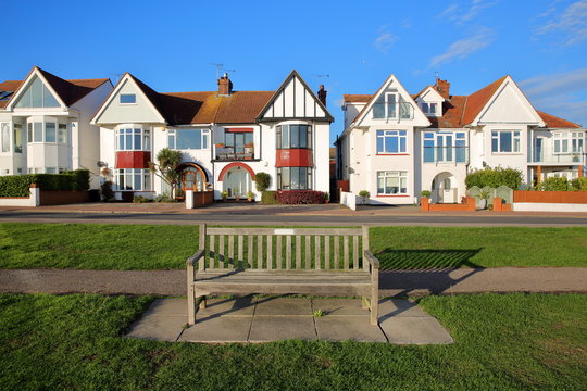 A row of colorful houses, located on Marine Parade, with a wooden bench in the foreground, Leigh on Sea, UK