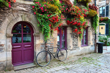 Vintage bicycle in front of the old rustic house, covered with flowers. Beautiful city landscape with an old bike near the stone wall with flowers in drawers in France, Europe. Retro style.