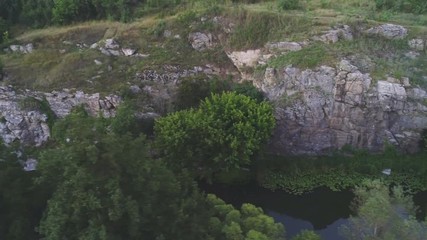 Mountain river flowing at a high rocky bank with leafy trees in in summer