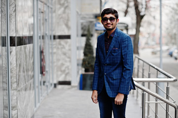 Young indian man on blue suit and sunglasses posed outdoor.