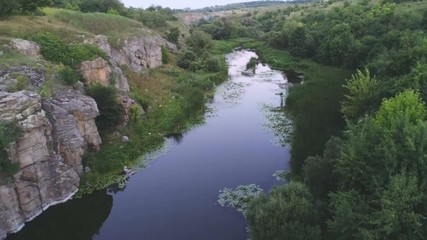 Thin river stretching between two rocky hills with wetland in summer