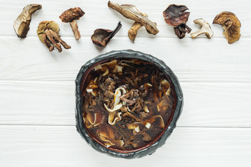 top view of traditional mushroom soup with dried mushrooms on white wooden background