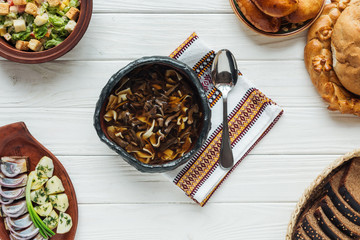delicious traditional mushroom soup with embroidered towel, spoon and dishes around on white wooden background