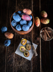 Blaue Zwetschgen und bunte Kaktusfeigen auf dunklem Holztisch mit Gewürzen