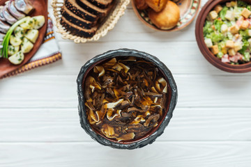 top view of delicious traditional mushroom soup and dishes around on white wooden background