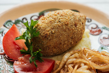 close up of chicken kiev with mashed potatoes, parsley, tomatoes and fried onions on plate with ornament