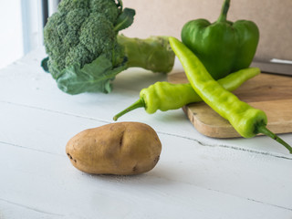 raw potato on white wooden table, blur brocoli and peppers backround,