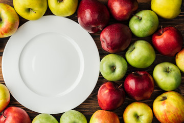 top view of white plate and multicolored apples on wooden table