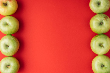 vertical frame of ripe green apples on red background